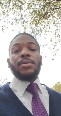 Howard environmental studies student dressed in a shirt and tie, poses for a selfie under a tree.
